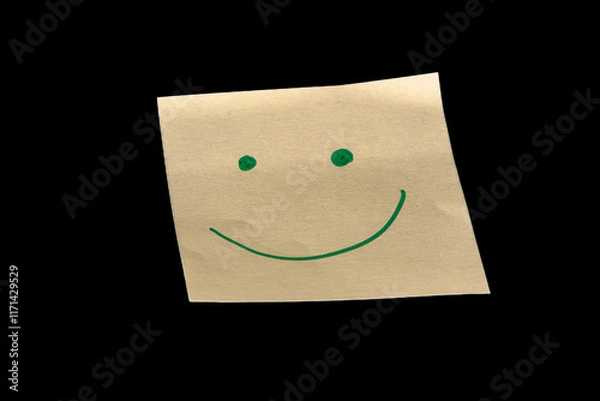 Fototapeta Yellow sticky note on a black background, featuring hand-drawn dots as eyes and an upward-curved line as a mouth, creating a joyful, happy, and calm expression