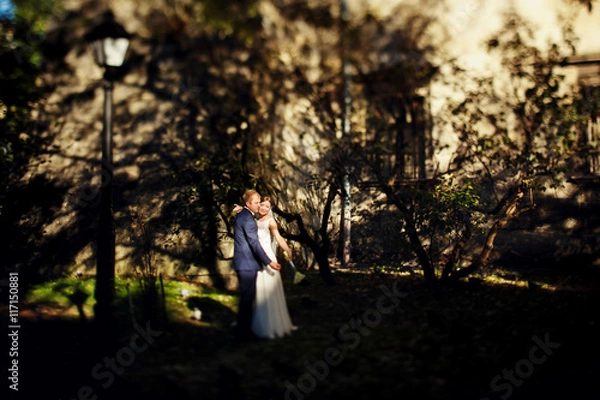 Fototapeta Bride reaches a hand with a bouquet out standing with a groom on