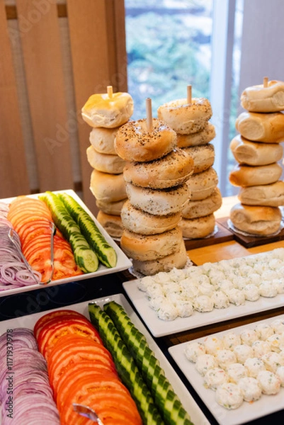 Fototapeta stacks of assorted bagels on wooden sticks and platters of cream cheese, tomatoes, cucumbers and onions at fancy bar mitzvah brunch