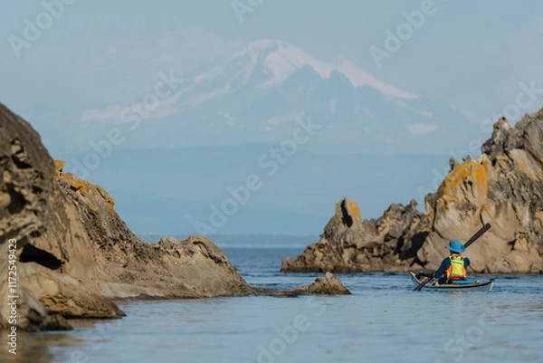 Fototapeta Woman kayaking along Sucia Island in the San Juan Islands in the Pacific Northwest in Washington with Mt Baker in background