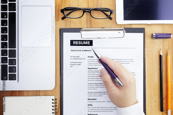 Fototapeta Businessman or HR Manager review a resume on his desk with Magnifier, computer laptop, digital tablet, calculator and glasses. Resume information with magnifier. Flat lay.