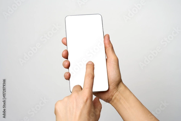 Fototapeta Finger touching phone on white background with copy space. Woman holding smartphone with white screen. Hand tap blank cellphone display, close-up