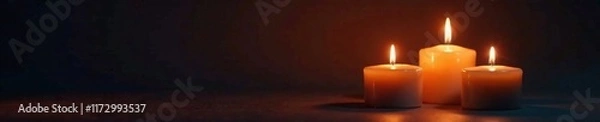 Fototapeta Soft warm glow of three burning candles on a dark background, abstract, shadows, light
