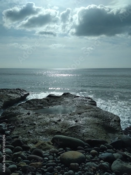 Fototapeta Beautiful sun shine on clouds and ocean on a summer day, in the foreground the beach with stones