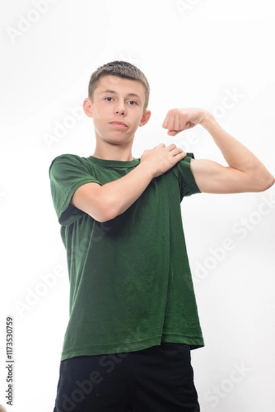Fototapeta A portrait of a young man in a green shirt flexing his arm. He displays a confident expression. The image is clean and simple, ideal for health or fitness concepts.