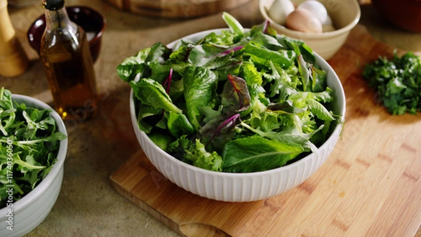 Fototapeta Close-up of a white bowl filled with fresh green salad made of lettuce leaves, with eggs and olive oil blurred in the background.