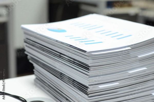 Fototapeta Stack of business reports on desk at workplace with high key tone.
