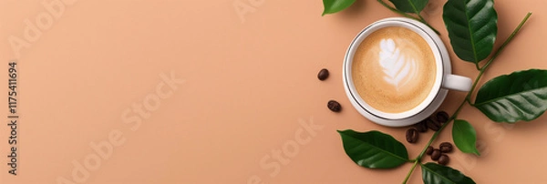 Obraz A white coffee cup with beautiful latte art rests on a light brown surface, surrounded by fresh green leaves and scattered coffee beans for an aesthetic touch.