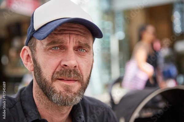 Fototapeta Hipster with beard and baseball cap sitting in a street cafe