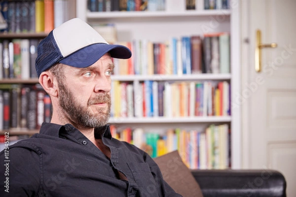 Fototapeta Man with beard and baseball cap sitting in a library