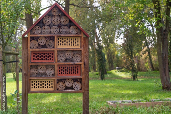 Fototapeta A handcrafted insect hotel in a lush green park, surrounded by trees, offers a glimpse into sustainable wildlife habitats. Perfect for projects on biodiversity, gardening, or eco-tourism.