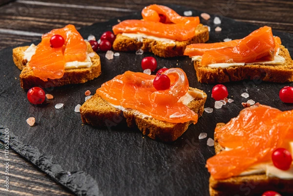 Fototapeta Delicious croutons with salmon and cranberries on a black board on the table