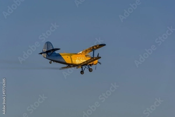 Obraz Crop duster spraying crops from the air in the morning light while turning to make another spraying run.