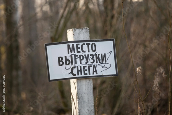 Fototapeta A sign on a wooden pole with the inscription in Russian "Snow dumping area" against the background of trees.