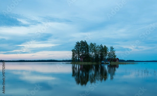 Fototapeta The island in the lake at sunset. The sky in the clouds. The smooth surface of the water.