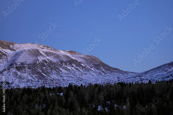 Fototapeta Montagne érodée et presque sans neige au printemps sous un ciel de fin du jour plongeant la vallée boisée dans la nuit.
