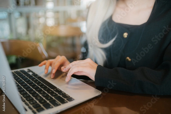 Fototapeta woman typing on laptop in cozy e setting, focused and engaged