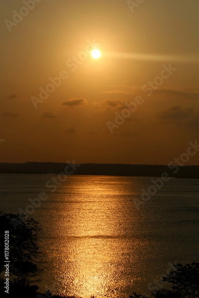 Obraz Sunset at the lagoon, with sunlight reflecting off the water, with the forest in the background, on the horizon