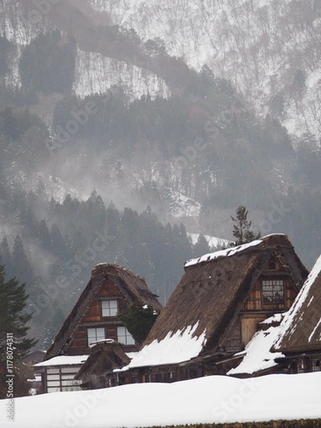 Obraz Traditional Gassho-style houses in Shirakawa-go, Japan, covered in snow with misty mountains in the background.