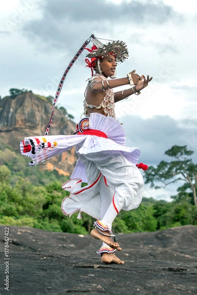Fototapeta SIGIRIYA, SRI LANKA - JULY 16, 2024 : A Ves Dancer, also known as a Kandyan Dancer or Up Country Dancer performs at Sigiriya in Sri Lanka. In the background stands Sigiriya Rock.