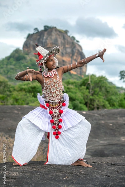 Fototapeta SIGIRIYA, SRI LANKA - JULY 16, 2024 : A Ves Dancer, also known as a Kandyan Dancer or Up Country Dancer performs at Sigiriya in Sri Lanka. In the background stands Sigiriya Rock.