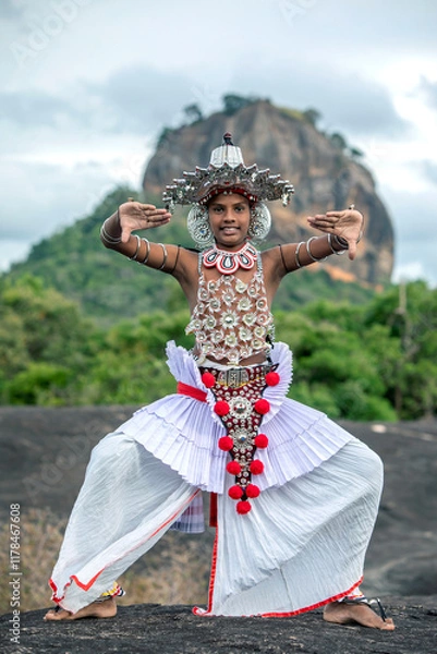 Fototapeta SIGIRIYA, SRI LANKA - JULY 16, 2024 : A Ves Dancer, also known as a Kandyan Dancer or Up Country Dancer performs at Sigiriya in Sri Lanka. In the background stands Sigiriya Rock.