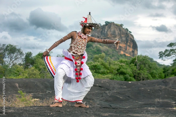 Fototapeta SIGIRIYA, SRI LANKA - JULY 16, 2024 : A Ves Dancer, also known as a Kandyan Dancer or Up Country Dancer performs at Sigiriya in Sri Lanka. In the background stands Sigiriya Rock.
