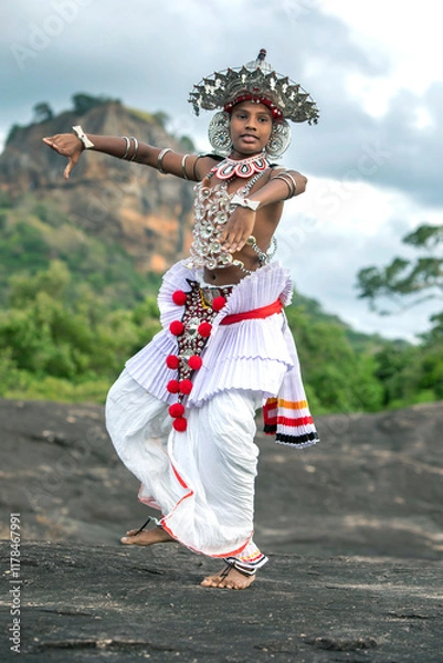 Fototapeta SIGIRIYA, SRI LANKA - JULY 16, 2024 : A Ves Dancer, also known as a Kandyan Dancer or Up Country Dancer performs at Sigiriya in Sri Lanka. In the background stands Sigiriya Rock.