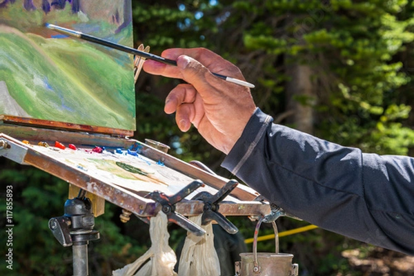Fototapeta Artist's Hand with Paint Brush Painting with an Oil Palette a Mountain Wildflower Landscape on Canvas on an Easel en Plein Air