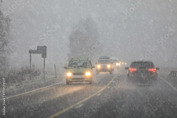 Obraz Driving in highway traffic with winter sleet and snow creating low visibility conditions, facing bright headlights of the oncoming traffic.
