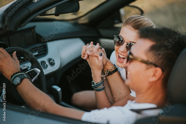 Obraz cheerful family couple lovers smiling and cheating to each other driving a cabriolet and searching the location they need by pointing on car gps system