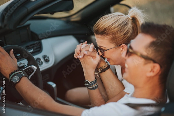 Obraz cheerful family couple lovers smiling and cheating to each other driving a cabriolet and searching the location they need by pointing on car gps system
