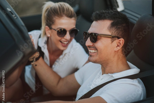 Obraz cheerful family couple lovers smiling and cheating to each other driving a cabriolet and searching the location they need by pointing on car gps system
