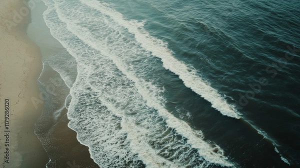 Fototapeta Soft waves roll onto a sandy beach as the sun sets in the background, casting a warm glow on the tranquil coastal landscape. The rhythm of the ocean creates a serene ambiance