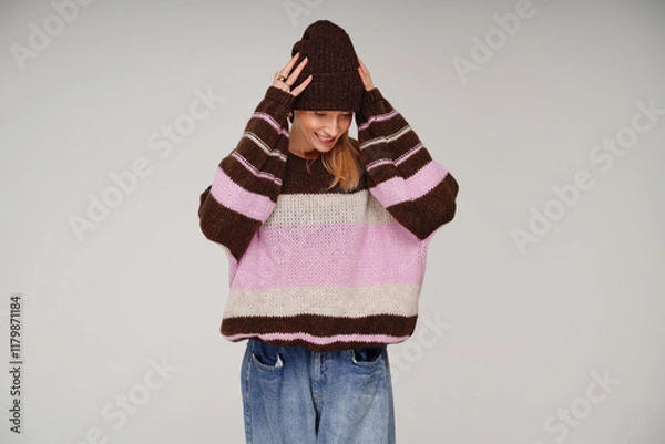 Obraz Portrait of cheerful woman in fashionable sweater and brown cap , posing in studio with delicate smile.