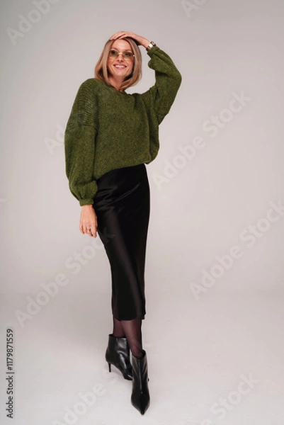Obraz Attractive female model wearing trendy sweater, midi skirt and boots, posing on studio background.