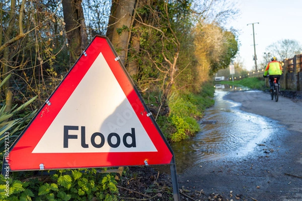 Fototapeta Flood Warning Sign With a Cyclist on a Flooded Road in the United Kingdom