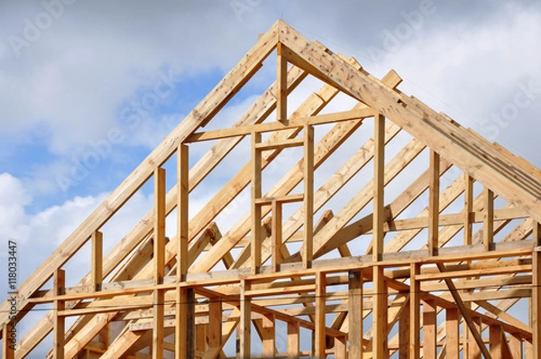 Fototapeta The process of construction of a frame private house with a pitched roof. Wooden frame on the blue sky background.