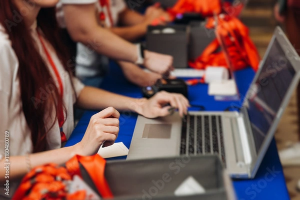 Fototapeta Process of checking in on conference congress forum event, registration desk table, visitors and attendees receiving lanyard with name badge and entry wristband bracelet and register electronic ticket