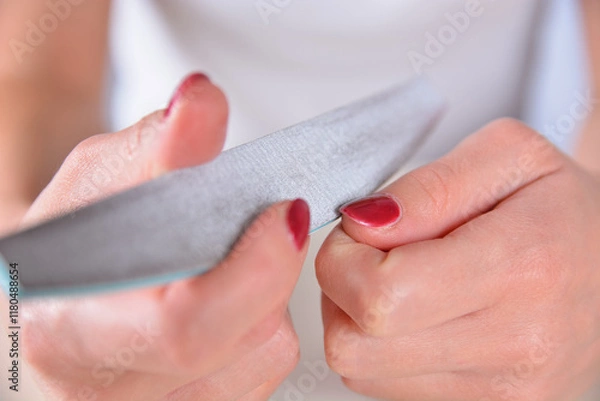 Fototapeta Close-up of a female hand filing red polished nails at home. Manicure and beauty concept