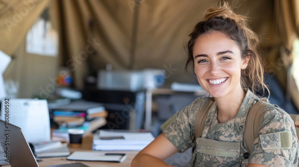 Fototapeta Australian woman in army uniform smiling, working with a laptop at tent