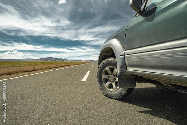 Fototapeta An off-road vehicle on mud tires stands on asphalt against the backdrop of the steppe, mountains and sky. Mud tires on asphalt in the steppe. A car for traveling. Rubber for travel.