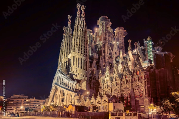 Fototapeta The Sagrada Família in Barcelona stands illuminated at night, showcasing Gaudí's breathtaking architectural brilliance with intricate carvings, soaring spires, and gothic-modernist design.