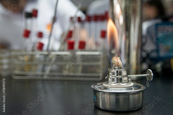 Fototapeta Close-up detail of an  ethanol burner, also known as a spirit lamp, in a microbiological laboratory with test tubes in the background. Science concept.