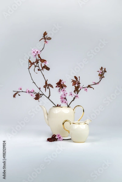 Fototapeta Still life with a pink blossoming branch in an elegant porcelain teapot with gold edging on a white background