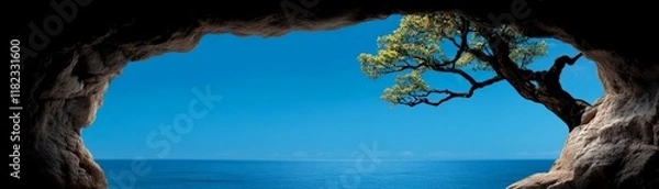 Fototapeta Cave to Ocean View: A picturesque view of a tranquil ocean seen through a dark cave opening, framed by rugged rocks and a lone tree, evokes a sense of serenity and hidden beauty. 
