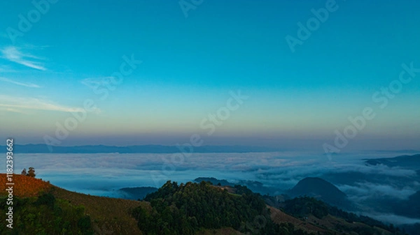Fototapeta A breathtaking aerial view of a mist-covered forest at sunrise. The dramatic cloudscape and soft fog create a serene and mystical atmosphere. Misty Sunrise Over Forested Hills with layers of mountain