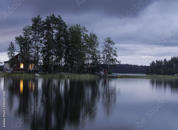 Fototapeta The island in the lake at sunset. The sky in the clouds. The smooth surface of the water.