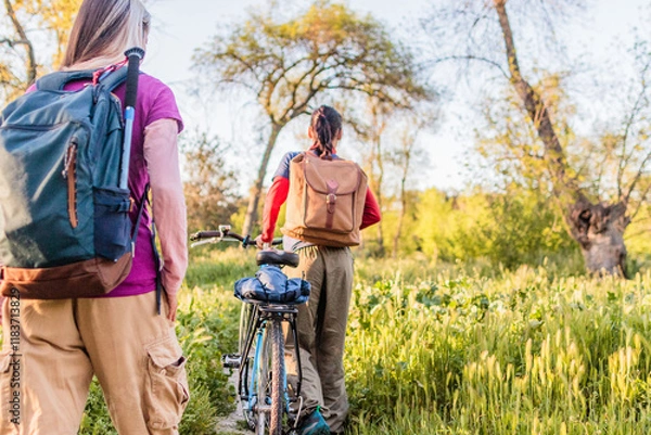 Fototapeta Hikers walking in nature with bicycle during golden hour