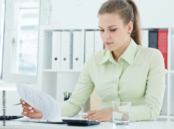 Fototapeta Beautiful young secretary .viewing entries in the papers on the clipboard sitting at office. 